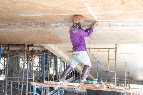 Builder worker with grinder machine polished finishing concrete ceiling at construction site.
