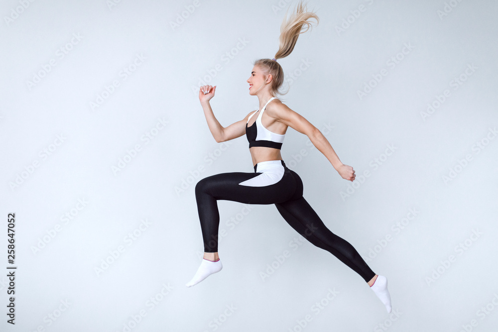 Full length fitness woman jumping agains gray background.