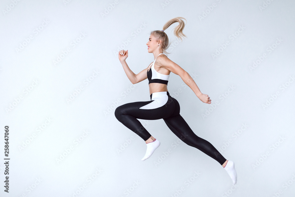 Fit young woman jumping against grey background. Female model in sports wear jumping.