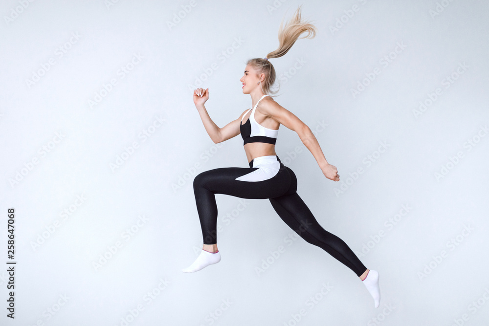 Full length fitness woman jumping agains gray background.