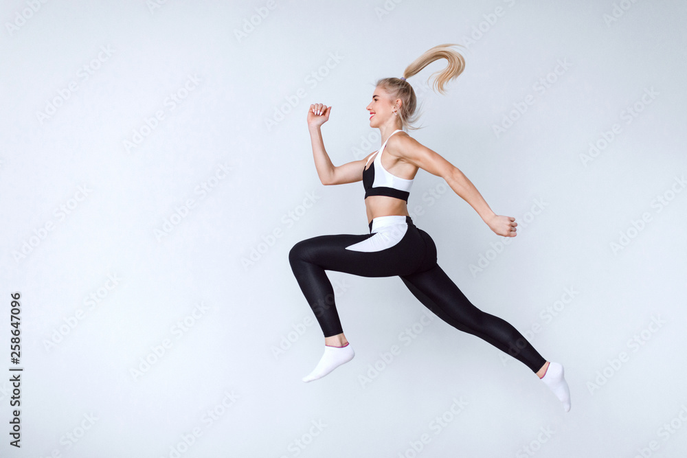 Fototapeta premium Fit young woman jumping against grey background. Female model in sports wear jumping.