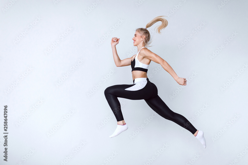 Fit young woman jumping against grey background. Female model in sports wear jumping.