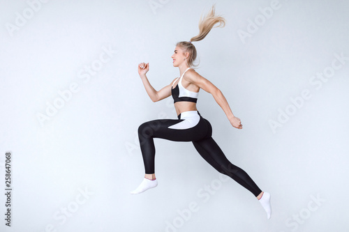 Full length fitness woman jumping agains gray background. © BestForYou