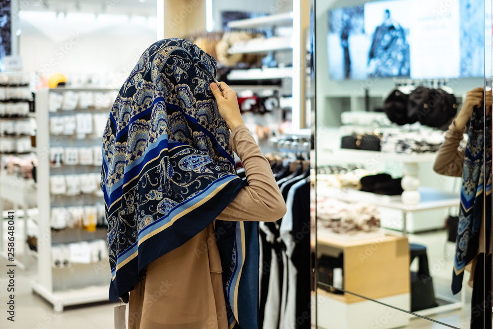 Thai muslim woman trying hijab in front of mirror at shopping mall. Selective focus. Shopping and fashio concept.