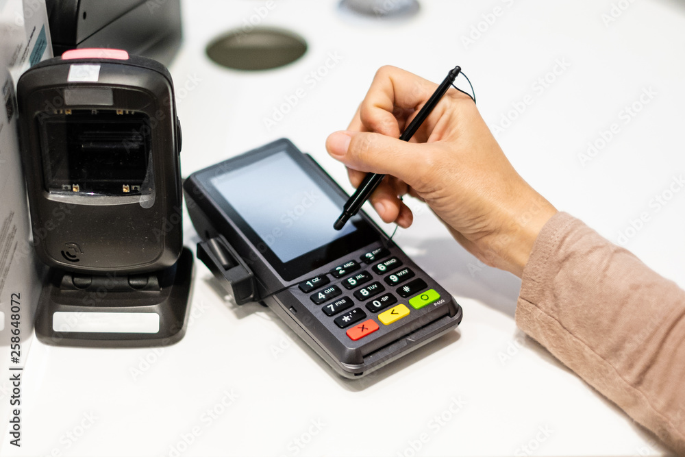 Close-up of consumer's hand signing on a touch screen of credit card sale transaction receipt machine. Close-up of consumer's hand signing on a touch screen of credit card sale transaction receipt machine.
