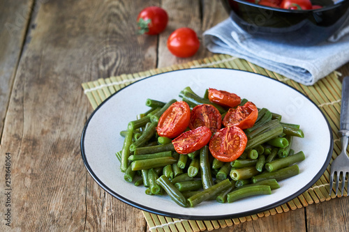 Green beans with baked cherry tomatoes on a wooden background