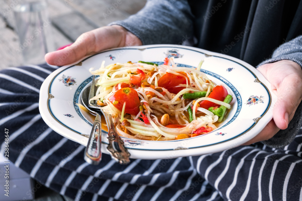 Woman's hand holding Thai green papaya salad in a dish, Somtam is very famous in Thailand. Thai spicy food Woman's hand holding Thai green papaya salad in a dish, Somtam is very famous in Thailand. Thai spicy food