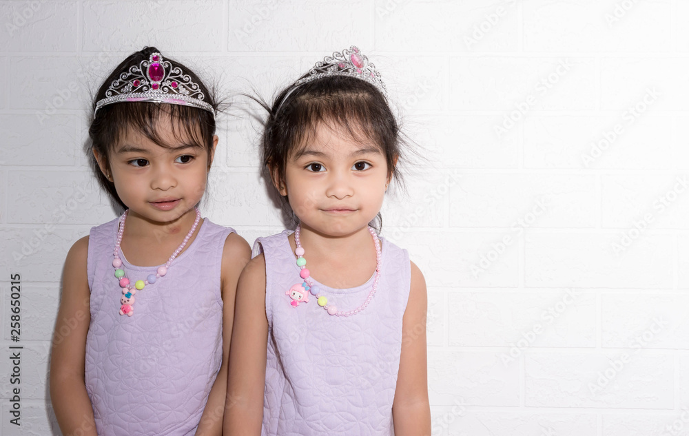 Female asian identical twins sitting on chair with white background. Wearing purple dress and accessories. Standing side by side each other Female asian identical twins sitting on chair with white background. Wearing purple dress and accessories. Standing side by side each other