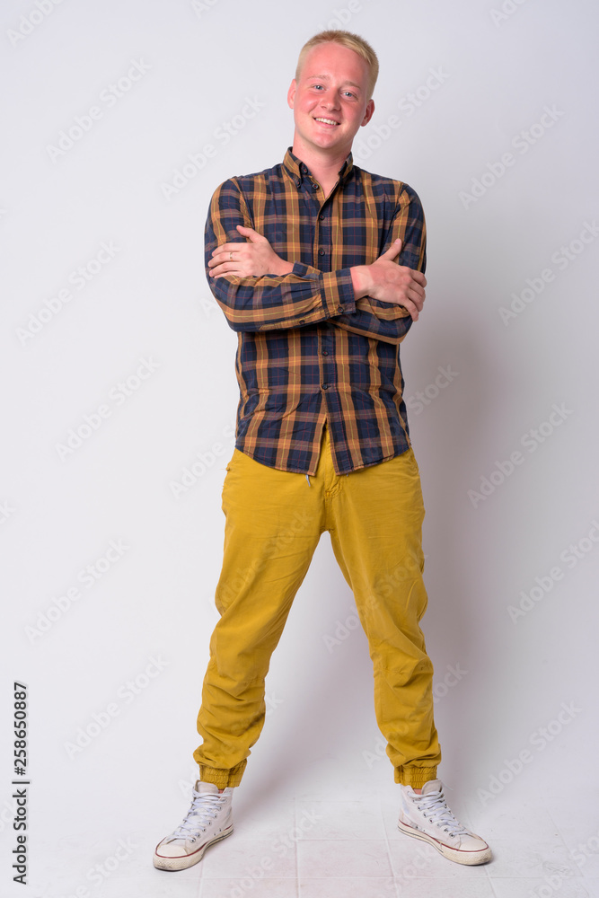 Full body shot of happy young blonde hipster man smiling with arms crossed