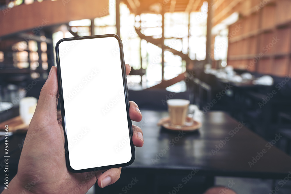 Mockup image of a man's hand holding black mobile phone with blank screen with a glass of coffee on wooden table in cafe Mockup image of a man's hand holding black mobile phone with blank screen with a glass of coffee on wooden table in cafe