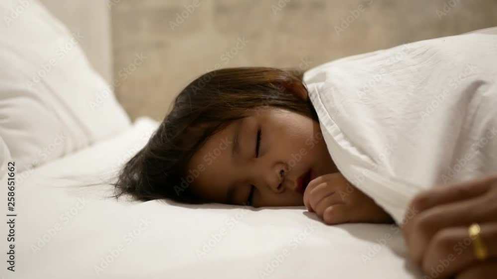 Asian mother is putting blanket on her daughter who is sleeping in the bed and goodnight kiss with love. Health care concept. Asian mother is putting blanket on her daughter who is sleeping in the bed and goodnight kiss with love. Health care concept.