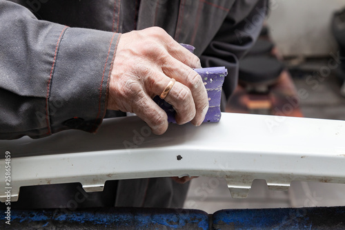 A man prepares a car body element for painting after an accident with the help of abrasive paper in a car repair shop. Recovery bumper after a collision.