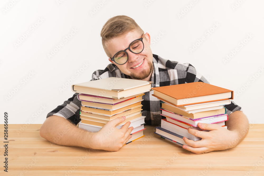 People, knowledge and education concept - smiling man sitting at the wooden table with books People, knowledge and education concept - smiling man sitting at the wooden table with books