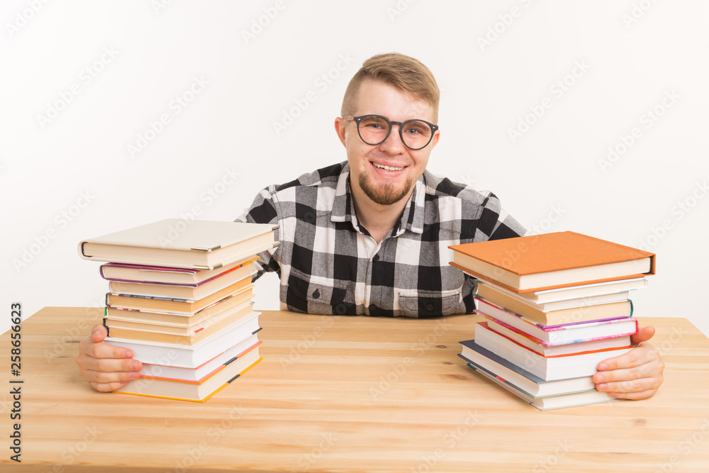People, knowledge and education concept - Happy funny student dressed in plaid shirt sitting at the wooden table with books People, knowledge and education concept - Happy funny student dressed in plaid shirt sitting at the wooden table with books