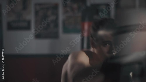 Cinematic shot of a young boxer training with the striking punching bag in the gym.