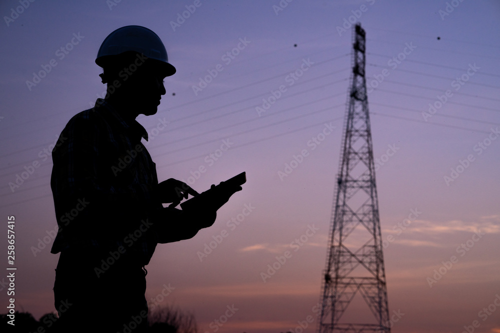 Silhouette of engineer standing orders by radio for construction crews to work safely on hi-voltage post. industry and safety at work concept. Silhouette of engineer standing orders by radio for construction crews to work safely on hi-voltage post. industry and safety at work concept.