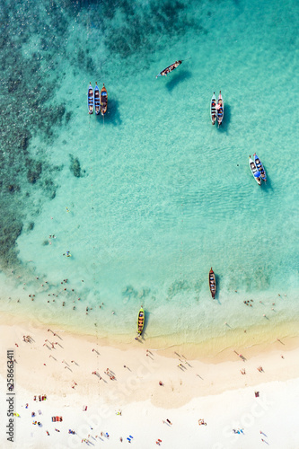 View from above, aerial view of a beautiful tropical beach with white sand and turquoise clear water, long tail boats and people sunbathing, Freedom beach, Phuket, Thailand. © Travel Wild