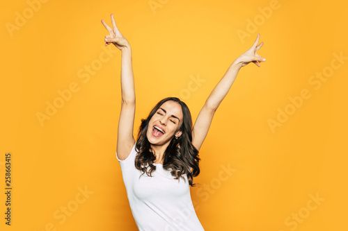 Are you ready?! A photo of vigorous young girl near the spicy-orange background showing “peace” sign to everyone and sending love through her emotions.