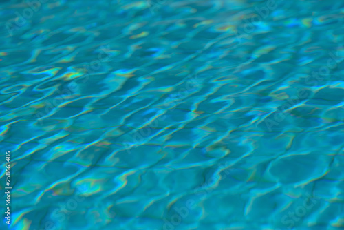 A swimming pool with a sunny reflection and beautiful wavy water surface in turquoise blue color with grab bars ladder on the sides and black line lanes underwater.