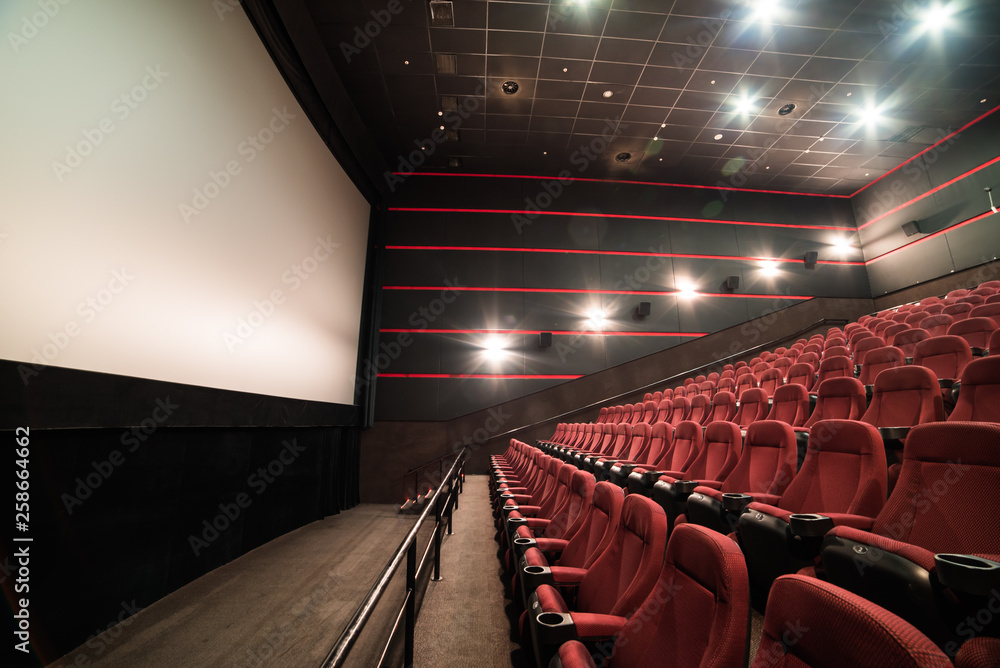 High-angle view of screen and rows of comfortable red chairs in illuminate red room cinema. Mock Up.