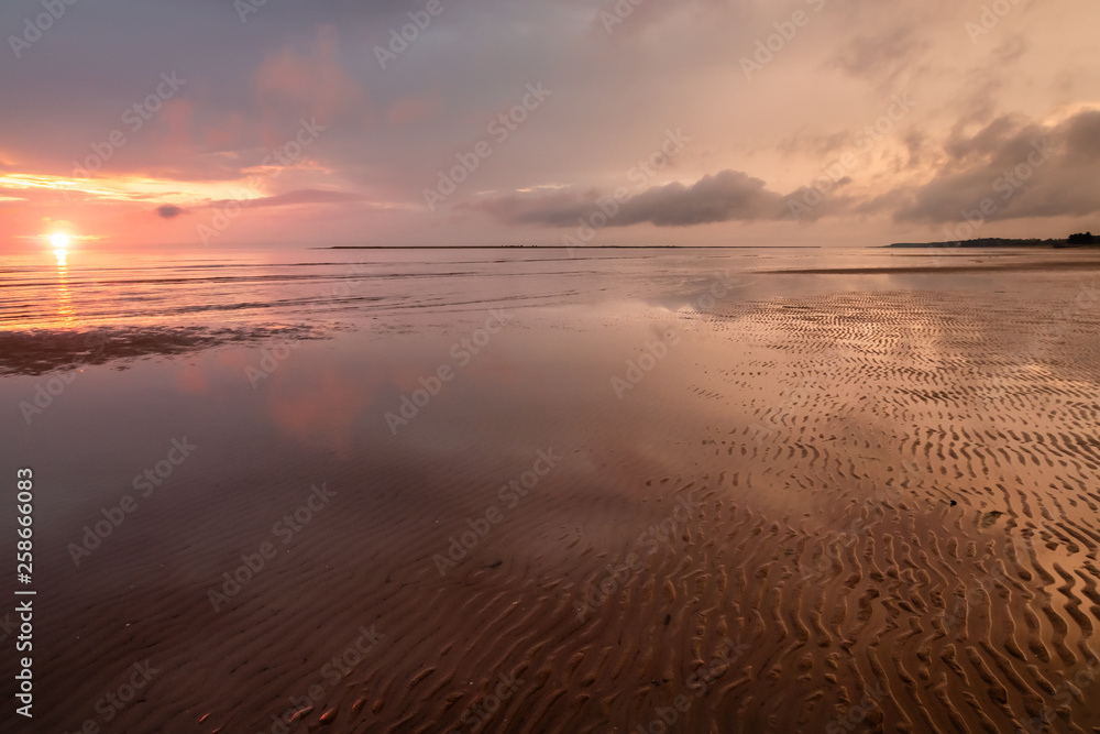 Beautiful sunset at the shore of a sea during low tide. Pinkish clouds reflected in the water. Serene summer landscape