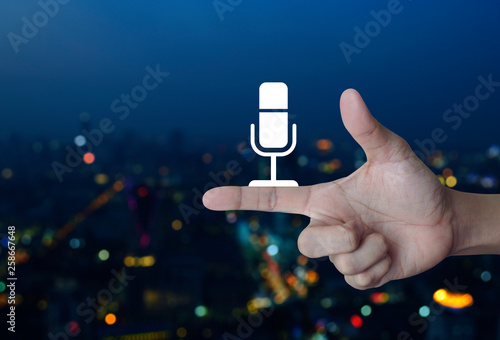 Microphone flat icon on finger over blur colorful night light city tower and skyscraper, Business communication concept