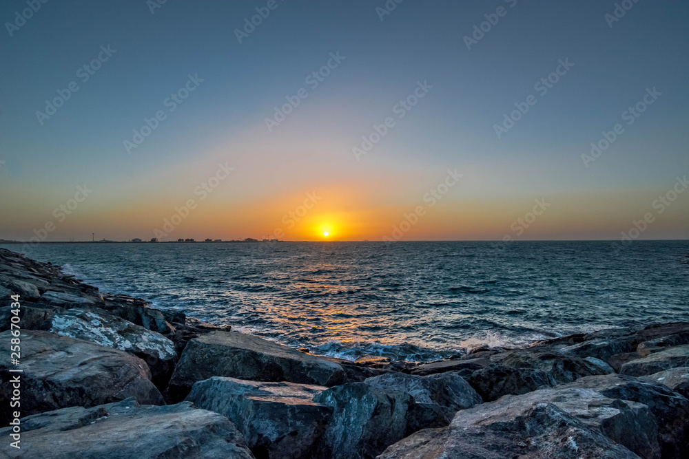 Beautiful Sun View in Beach from rock stone island shore with orange sky and yellow light reflection on sea water waves