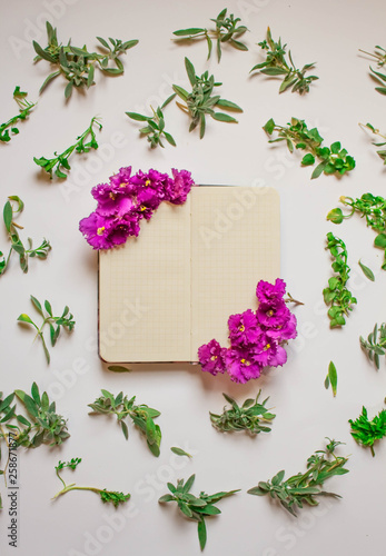 Empty notebook decorated purple flowers on a white background, top view. Notepad decorated with green leaves and violet. Flat lay.