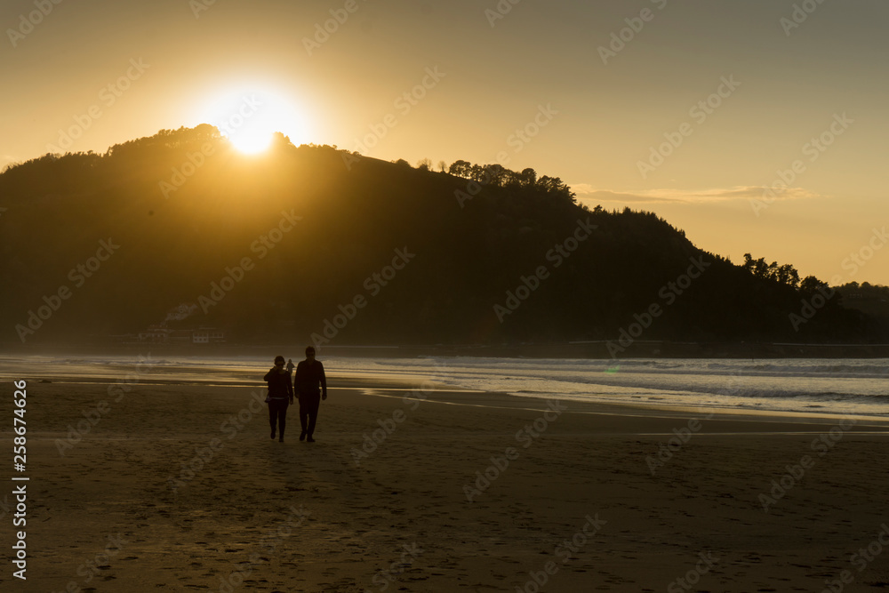 Dos personas paseando por la playa al atardecer en Zarrautz