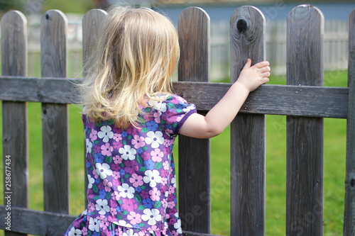 A child holding a fence and looking over at the other side. 