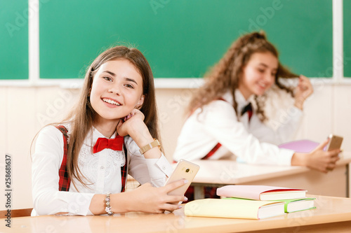 two beautiful schoolgirls are sitting at the desk with books in the classroom