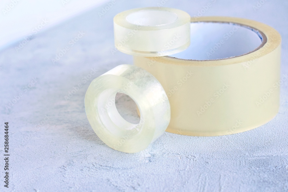 Set of glue packing tape with selective focus on grey cement background.  Repair plastic tapes on neutral surface. Bobbin with transparent sticky  sellotape. Fix or packaging tapes Stock Photo | Adobe Stock