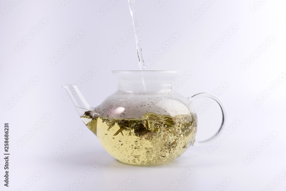 Pouring hot water to the glass teapot with herbal tea, isolated on white background Pouring hot water to the glass teapot with herbal tea, isolated on white background