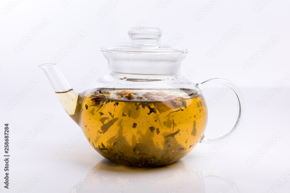 Glass teapot with herbal tea and roses isolated on white background