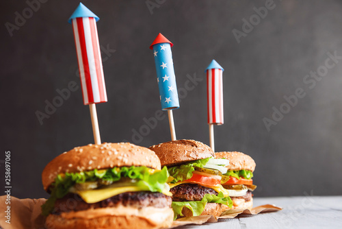 three fresh and juicy burgers with American flag-style fireworks inserted into them. bbq concept picnic to celebrate independence day