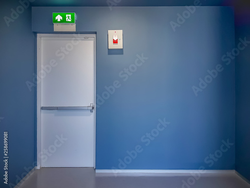 Fire exit door and emergency red light alarm box on blue wall in modern style building.