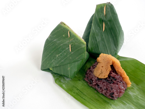 Thai fevorite dessert,Black sticky rice topping with egg custard wrapped in banana leaf packag,Isolated image. photo