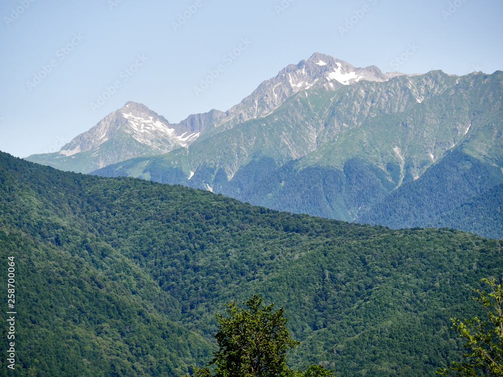 High mountains with green slopes with snowy peaks. Snow and green grass on the mountain slopes in summer.