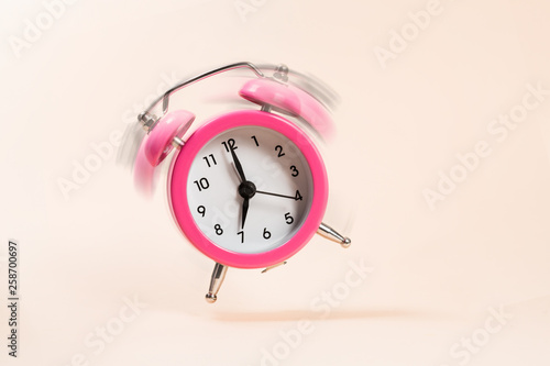 Pink bouncing ringing alarm clock on a beige background. Motion blur.