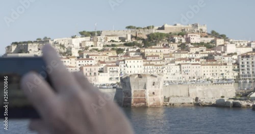 Man with phone taking pictures of Town on island Ebla port in Italy photo