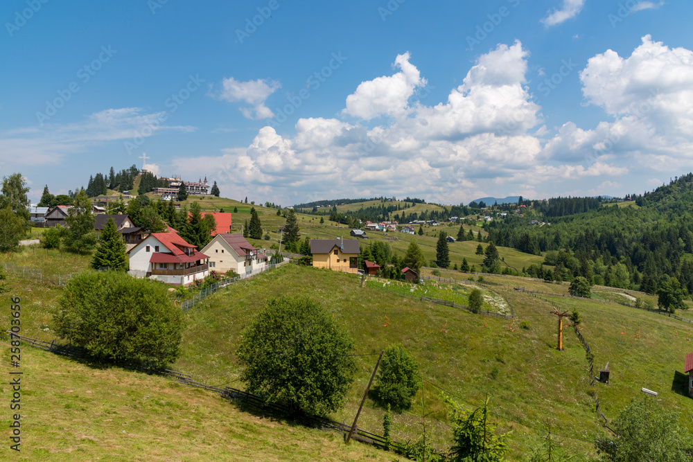 Beautiful countryside in romana, farms and old wooden houses with gardens. Cabins and barns at the foot of the mountains. Cloudy blue sky. Lawns and forests