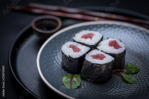 maki sushi raw tuna nori seaweed with soy sauce and chopsticks on a dark plate