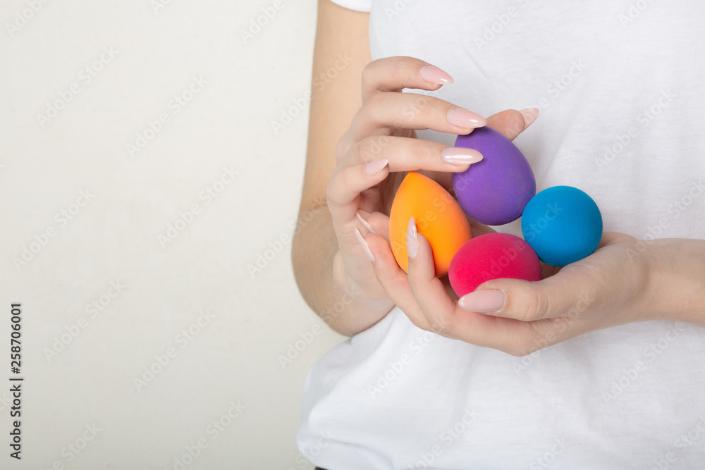 Naklejka premium Woman with nice manicure holding colorful beauty blenders. Empty space