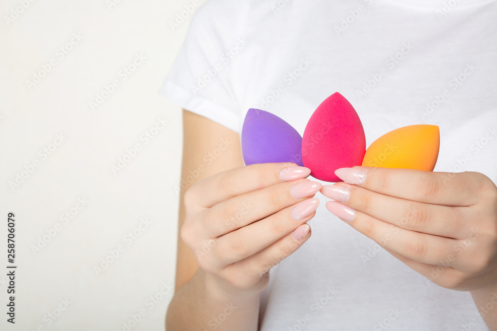 Female hands with pretty manicure holding purple, pink and orange cosmetic sponges. Space for text Female hands with pretty manicure holding purple, pink and orange cosmetic sponges. Space for text