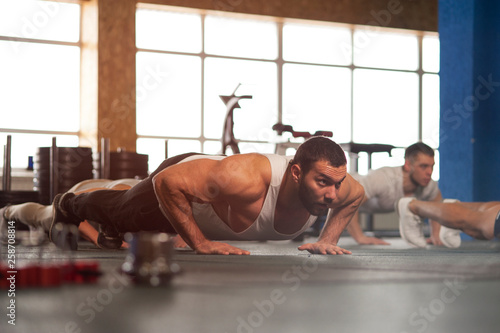 Small Group of Muscular Male Adults Warming Up Training Push Ups.
