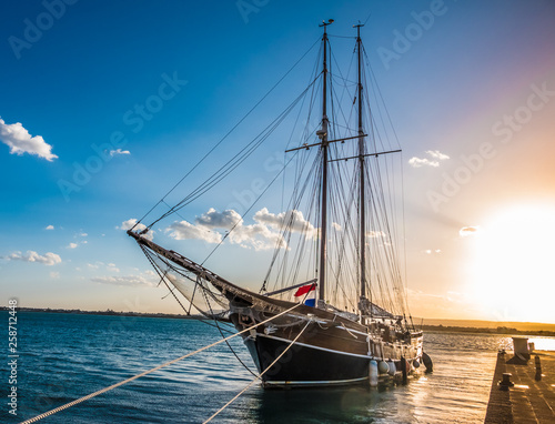 An elegant tall ship among the colorful variety of boats and ships fill the docks of the harbors of Syracuse (Siracusa), a historic city on the island of Sicily, Italy.
