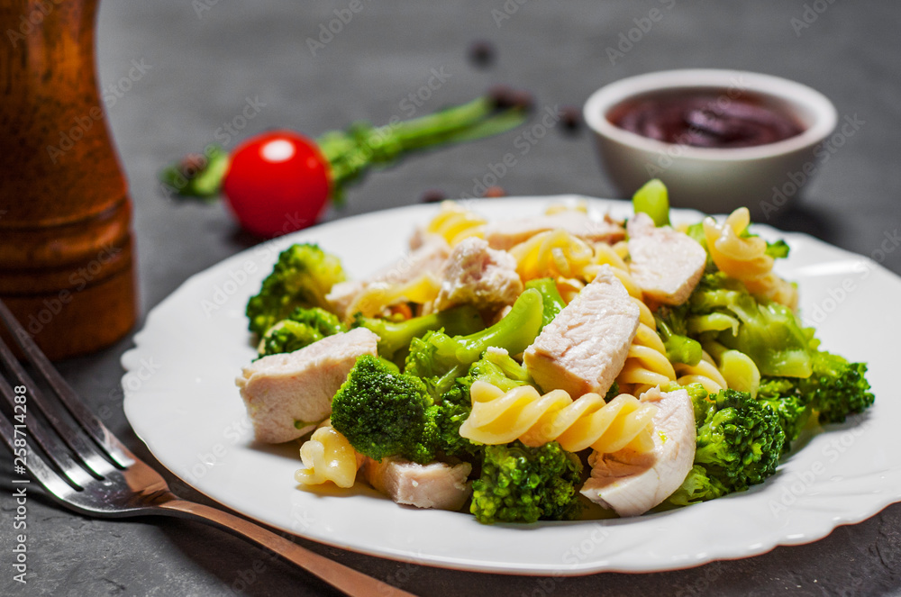 fusilli pasta with chicken breast and broccoli salad in white plate on Dark grey black slate background fusilli pasta with chicken breast and broccoli salad in white plate on Dark grey black slate background