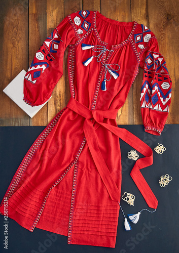 Beautiful unusual outfit presentation for fashion blog, advertising, clothing catalog. Red long dress with a pattern in Russian, Ukrainian, Belarusian, European, Slavic style. Book and other decor.