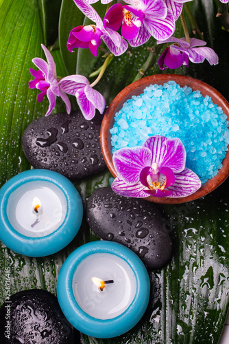 bowl with lavender-scented bath salt, orchid, massage stones, covered with water drops, and scented candles.