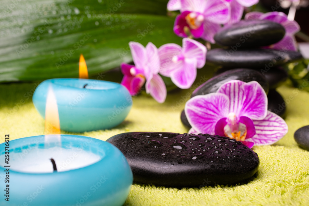 spa concept. a lit candle in the foreground, and stones with orchids in the background spa concept. a lit candle in the foreground, and stones with orchids in the background